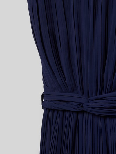 Mädchen trägt Regular Fit Jumpsuit in Plissee-Optik von DANAMADE, Zierschleife, taillierte Passform, Nahaufnahme Oberkörper.
