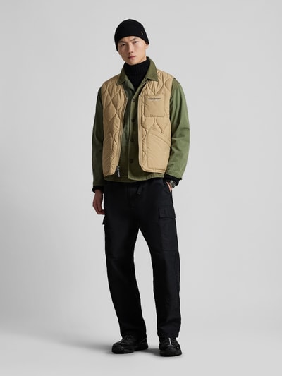 Männermodel trägt Regular Fit Steppweste mit Brusttasche van Polo Ralph Lauren in beige, uni, V-hals, borstzak, steekzakken, label stitching, ganzkörperansicht von vorne.
