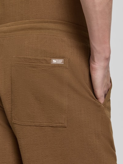 Männermodel trägt Relaxed Fit Sweatshorts aus reiner Baumwolle Modell 'DETROIT' von s.Oliver RED LABEL, braun, fein strukturiert, Gesäßtasche, Nahaufnahme Hüfte.
