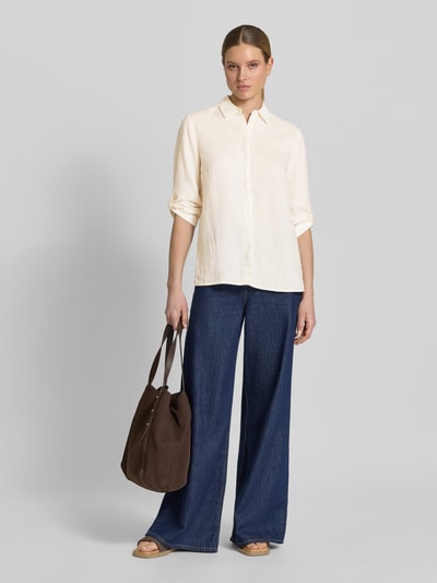 Modelka kobieca ma na sobie Relaxed Fit Leinenbluse mit 3/4-Arm Modell 'Clay' od TONI, beżowy len, koszulowy kołnierz, zasłonięta listwa guzikowa, długość tyłu 63 cm, długość rękawa 36 cm, szerokie niebieskie spodnie, brązowa torebka, naturalna faktura tkaniny, pełen widok z przodu.