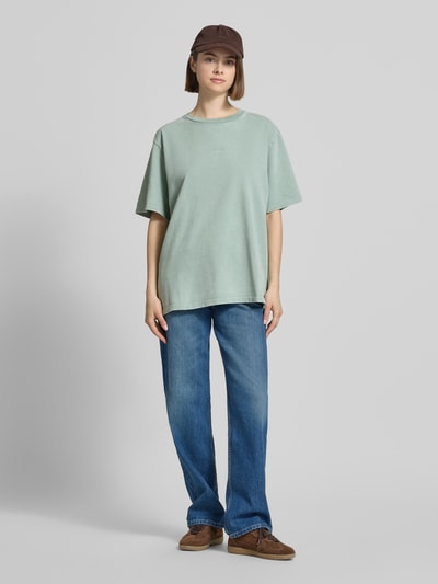 Frauenmodel trägt Damen T-Shirt von OH APRIL aus Reine Baumwolle, Oversized, Modell 'Farmers Market', Rundhalsausschnitt, Label-Stitching, Rückenlänge bei Größe S 69 cm, blasses Grün, lockere Form, glatte Textur, Ganzkörperansicht von vorne.