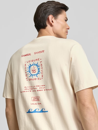 Mężczyzna nosi T-shirt z label-print Modell 'GERGEI' od Samsøe Samsøe z czystej bawełny, krój relaxed fit, kolor beżowy, nadruk na plecach, okrągły dekolt, długość tyłu w rozmiarze M: 71 cm, całkowity widok z tyłu.