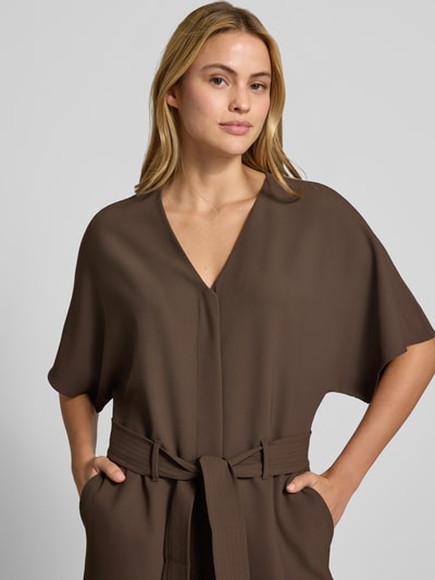 Kobiece modelka nosi kombinezon Jumpsuit mit V-Ausschnitt Modell 'Lehila' od MOS MOSH, dekolt w serek, krój taliowany, rękaw o dł. 1/2, Długość tyłu w rozmiarze S: 46 cm, Szerokość w rozmiarze S: 50 cm, Długość rękawów w rozmiarze S: 40 cm, całkowita długość w rozmiarze S: 149 cm, Długość wewnętrzna nogawki w rozmiarze S: 76 cm, kolor brązowy, gładka tekstura, zbliżenie na górną część ciała.