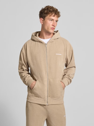 Männermodel trägt Oversized Fit Sweatjacke mit Label-Detail Modell 'Mezzano' von PEGADOR in Beige, Material-Mix, Ganzkörperansicht von vorne. Rückenlänge 70 cm, Ärmellänge 68 cm, elastische Abschlüsse, getrennte Känguru-Tasche.