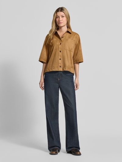 Kobiece model prezentuje bluzkę z krótkim rękawem 'Bluse mit Brusttaschen und Logo-Prägung' od Smith and Soul, mieszanka materiałów z dodatkiem streczu, krój loose fit, kołnierzyk typu kent, listwa guzikowa, kieszenie na piersi, wytłoczone logo, długość tyłu w rozmiarze S: 58 cm, długość rękawów w rozmiarze S: 27 cm, kolor brązowy, faktura gładka, całkowity widok z przodu
