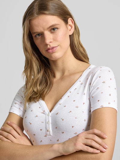 Vrouwenmodel draagt Cropped T-shirt met V-hals en knoopsluiting van Guess Jeans in wit met materiaalmix met viscose, logoprint, nahaufnahme bovenlichaam.