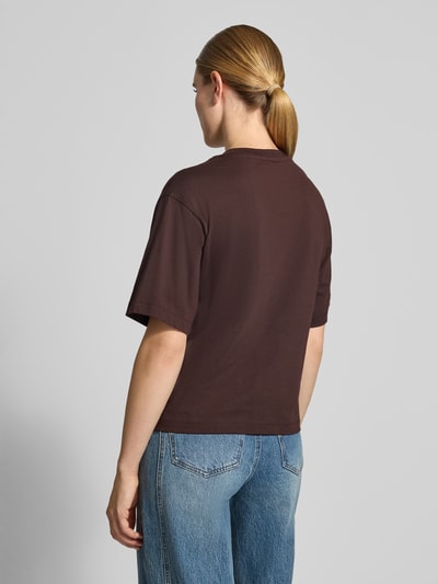 Vrouwenmodel draagt oversized fit t-shirt uit puur katoen met geborduurd logo en bloemenborduursel van closed, halflange mouwen, ruglengte maat S 52 cm, oversneden schouders, effen bruin, rechte vormen, gladde textuur, ganzebovenaanzicht rugaanzicht.