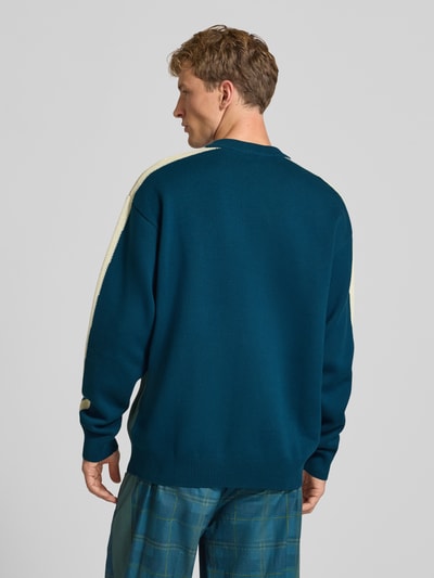 Męski model nosi Relaxed Fit Pullover aus Baumwoll-Mix od PUMA Performance w kolorze niebieskim z jasnymi paskami, widok całej sylwetki od tyłu.