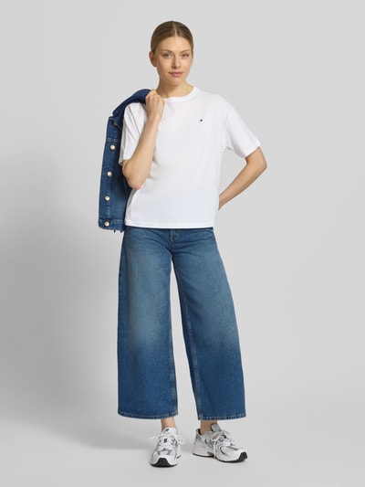 Frauenmodel trägt Slim Fit T-Shirt aus reiner Baumwolle von TOMMY HILFIGER, Optik: Unifarben, Passform: Slim-Fit, Logo-Stitching, Rundhals, Ärmelform: Kurzarm, Materialverarbeitung: Jersey, Material: Reine Baumwolle in Weiß, glatte Textur, Ganzkörperansicht von vorne.