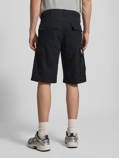 Mannenmodel draagt Shorts mit Cargotaschen van Carhartt Work In Progress in regular fit, donkerblauw, cargozakken, achterzakken, bandwijdte 43 cm, binnenbeenlengte 29 cm, volledige achteraanzicht.