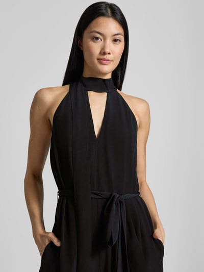 Frauenmodel trägt Regular Fit Jumpsuit aus reiner Viskose Modell 'Chiva' von Ted Baker in Schwarz mit Schlüssellochausschnitt, Nahaufnahme Oberkörper. Damen Jumpsuit, ärmellos, taillierte Passform, Zierschleife, glatte Textur.
