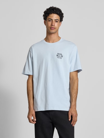 Männermodel trägt Relaxed Fit T-Shirt aus reiner Baumwolle Modell 'MILO' von Only & Sons, unifarben, Schriftzug-Print, Rundhals, Kurzarm, Ganzkörperansicht von vorne.