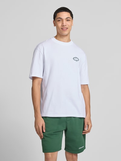 Męski model nosi Oversized T-Shirt mit rückseitigem Motiv-Print Modell 'Reine' von Pegador z białej bawełny, nadruk z logo, krój oversized fit, okrągły dekolt, długość tyłu 70 cm w rozmiarze M, widok całej sylwetki z przodu.