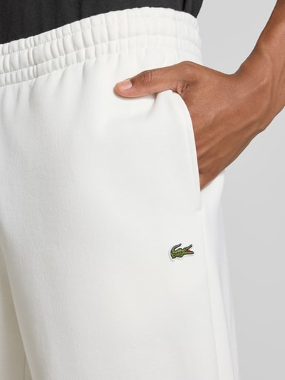 Männermodel trägt Regular Fit Sweathose aus Baumwoll-Mix von Lacoste in Weiß mit eingesticktem Logo, Nahaufnahme Oberschenkel. Herren Sweathose von Lacoste.