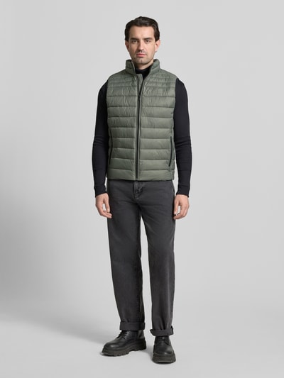 Männermodel trägt Regular Fit Steppweste mit Stehkragen Modell 'ODENO2' von BOSS Orange in Oliv, unifarben, Ganzkörperansicht von vorne.