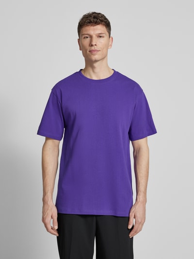 Männermodel trägt ein unifarbenes lila Relaxed Fit T-Shirt aus Bio-Baumwoll-Mix Modell 'MAARKOS' von Armedangels, Ganzkörperansicht von vorne.