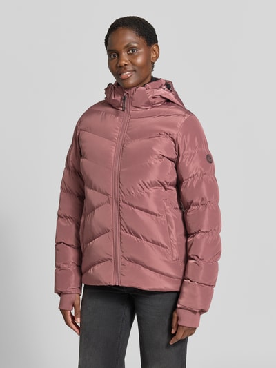 Kobieta nosi kurtkę pikowaną w kolorze różowym, model 'Synria' marki Cars Jeans, krój regular fit, kaptur ze stójką, wpuszczane kieszenie, zamek błyskawiczny, długość tyłu w rozmiarze S: 65 cm, szerokość ramion w rozmiarze S: 42 cm, szerokość w rozmiarze S: 50 cm, długość rękawów w rozmiarze S: 70 cm, zdjęcie całej sylwetki z przodu.