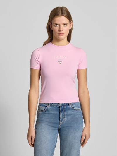 Vrouwenmodel draagt T-shirt met logo en ronde hals van Guess Jeans, roze kleur, slim fit, katoen-elastaan mix, voorkant, bovenlichaam close-up.