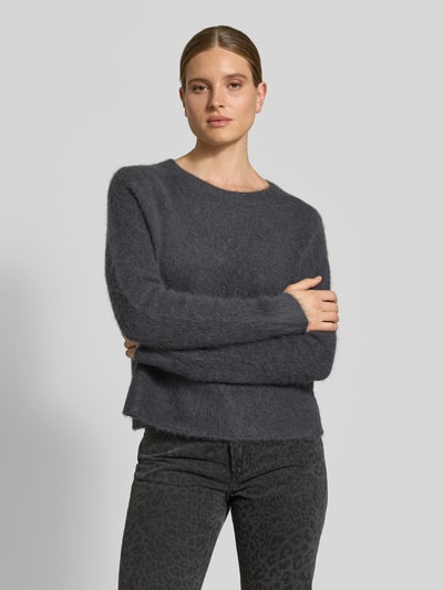 Vrouwenmodel draagt Wollpullover aus Alpaka-Woll-Mix van Juvia in donkergrijs met tricotlook, los model, ronde hals, elastische mix van alpaca en wol, ruglengte maat S 57 cm, borstwijdte 50 cm, mouwlengte 62 cm, oversneden schouders, gebreide textuur, fijne melange, ganzlichaamsaanzicht van voren.