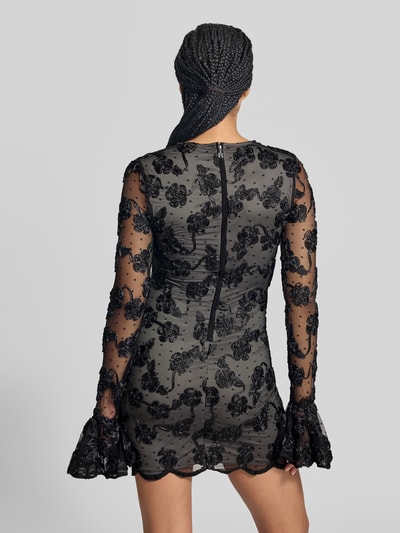 Frauenmodel trägt Minikleid mit floralem Besatz von ROTATE, schwarze Spitze, blickdichtes Unterkleid, langärmelig, Ganzkörperansicht Rückansicht.