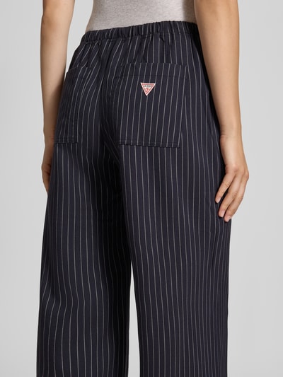 Vrouwenmodel draagt Wide Fit broek met elastische band van GUESS, donkerblauw met witte strepen, bandplooien, detailopname van achteren.