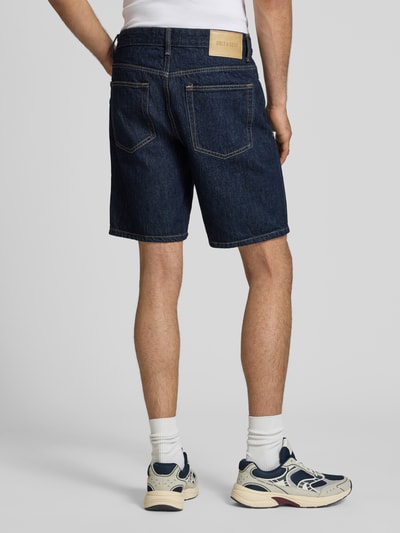 Männermodel trägt Regular Fit Jeansshorts aus reiner Baumwolle Modell 'EDGE' von Only & Sons in dunkler Denim-Optik, Twill Materialverarbeitung, Label-Patch, 5-Pocket-Design, Ganzkörperansicht Rückansicht.