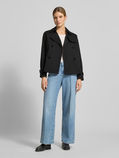 Modelka nosi Trenchcoat mit Knopfverschluss od MICHAEL Michael Kors, czarny, krój regular fit, kołnierz wykładany, dwurzędowy, długość pleców w rozmiarze S: 61 cm, szerokość ramion w rozmiarze S: 40 cm, szerokość w rozmiarze S: 52 cm, długość rękawa w rozmiarze S: 63 cm, gładka faktura, widok całej sylwetki z przodu.