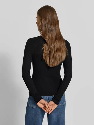 Frauenmodel trägt Slim Fit Pullover mit Woll-Anteil von MYON, schwarzer Material-Mix, Stehkragen, feines Lochmuster, Ganzkörperansicht Rückansicht.