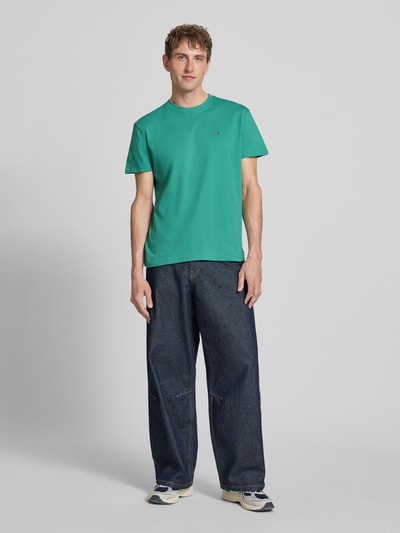 Männermodel trägt Regular Fit T-Shirt aus reiner Baumwolle von Tommy Jeans in Unifarbe, Rundhals, kurzarm, Logo-Stitching, Ganzkörperansicht von vorne.
