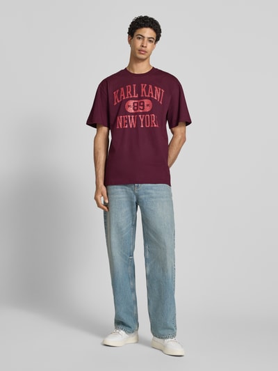 Männermodel trägt Oversized Fit T-Shirt mit Logo-Print Modell 'Heritage' von KARL KANI in Dunkelrot, Reine Baumwolle, Rundhalsausschnitt, Rückenlänge bei Größe M 73 cm, Herren T-Shirt, Ganzkörperansicht von vorne.