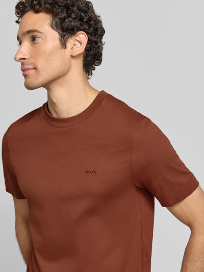 Männermodel trägt T-Shirt mit Rundhalsausschnitt von BOSS in Braun, unifarben, kurzarm aus reiner Baumwolle, Logo-Schriftzug, Nahaufnahme Oberkörper.