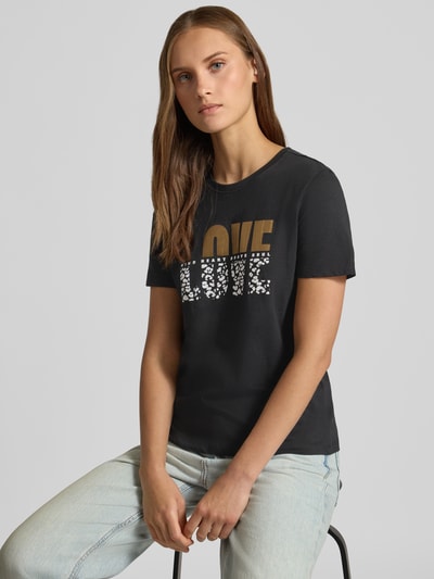 Kobiece model prezentuje damski t-shirt Regular Fit T-Shirt aus reiner Baumwolle Modell 'KITA' von ONLY w kolorze czarnym z nadrukiem, tekstura gładka, z przodu napis, damski t-shirt od ONLY, zbliżenie na górną część ciała.