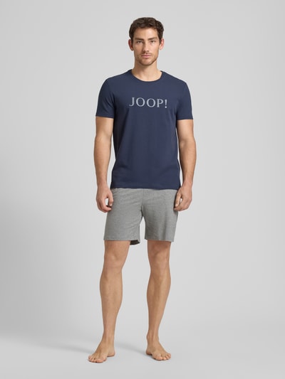 Männermodel trägt Sweatshorts mit elastischem Bund und Kordelzug von JOOP! Collection in Hellgrau, lockerer Schnitt, Ganzkörperansicht von vorne. Baumwoll-Mix mit Stretch-Anteil und sichtbarem Kordelzug.