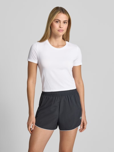 Kobiece modelka nosi damski t-shirt Cropped T-Shirt mit Rundhalsausschnitt Modell 'Feather' od Fabletics, elastyczna mieszanka materiałów, krój krótki, okrągły dekolt, długość tyłu w rozmiarze S: 45 cm, widok całego ciała z przodu.