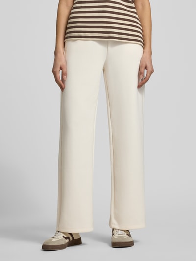 Modelka nosi spodnie dresowe Sweatpants mit elastischem Bund od ARMANI EXCHANGE, mieszanka wiskozy i elastanu, krój relaxed fit, paski w kontrastowym kolorze, beżowe tło, długość wewnętrzna nogawki w rozmiarze S: 77 cm, całkowity widok z przodu