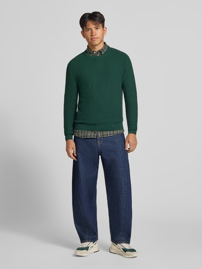 Männermodel trägt Regular Fit Pullover aus reiner Baumwolle Modell 'TONY' von ONLY & SONS, dunkles Grün, glatte Struktur, Ganzkörperansicht von vorne.