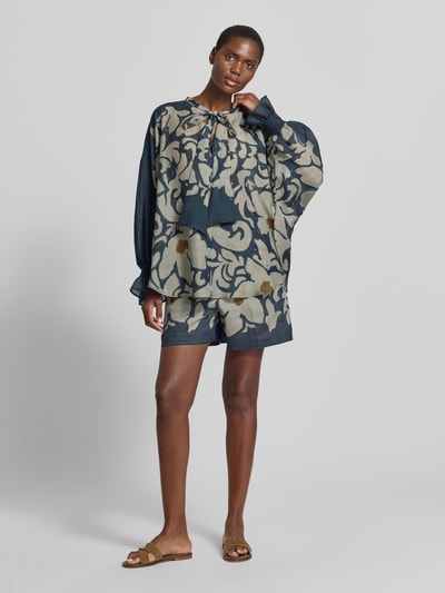 Modelka nosi Bluse mit Schluppe und Volantärmeln von Luisa Cerano, mieszanka lyocellu z dodatkiem ramii, krój loose fit, wycięcie w kształcie łezki z kokardą, rękawy z falbanami i marszczonym detalem, długość tyłu w rozmiarze 36: 74 cm, długość rękawów: 65 cm, wzór w odcieniach niebieskiego, beżowego i żółtego, tekstura lekko transparentna, cała sylwetka z przodu.
