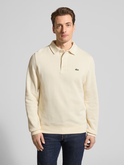 Męski model nosi Regular Fit Sweatshirt aus reiner Baumwolle od Lacoste, jasny beż, gładka faktura, kołnierz polo, długi rękaw, krój regular fit, logo, bawełna, widok całej sylwetki z przodu.