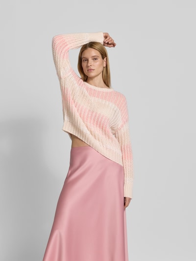 Frauenmodel trägt Relaxed Fit Pullover mit Alpaka-Anteil von Juvia in Strick-Optik mit Lochmuster, creme und rosa, Nahaufnahme Oberkörper.