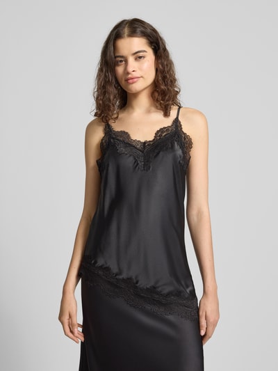 Frauenmodel trägt Slim Fit Trägertop mit Spitzenbesatz Modell 'JESSA' von PIECES, Farbe Schwarz, Optik: Unifarben, V-Ausschnitt, Satin, verstellbare Spaghettiträger, asymmetrischer Rumpfabschluss, Ganzkörperansicht von vorne.