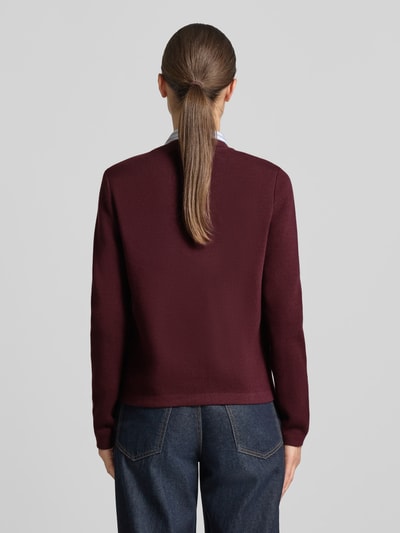 Frauenmodel trägt Regular Fit Strickjacke aus reiner Baumwolle von GANT in Dunkelrot, kombiniert mit blauer Jeans, Ganzkörperansicht Rückansicht, Damen Strickjacke von GANT.