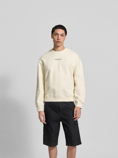 Männermodel trägt Hoodie aus Baumwoll-Mix von MAISON KITSUNÉ in Creme mit Label-Stitching, lockere Passform, Ganzkörperansicht von vorne.