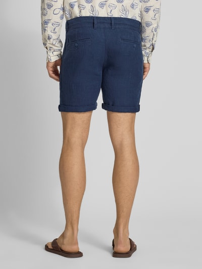 Mężczyzna nosi Leinenshorts mit Bindegürtel und Gesäßtaschen von MCNEAL, granatowy len, krój straight fit, zakładka, długość wewnętrzna nogawki 16 cm, szerokość w rozmiarze M 45 cm, wpuszczane kieszenie, haftowane logo, widok całej sylwetki z tyłu.