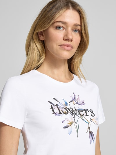 Frauenmodel trägt T-Shirt mit Strasssteinbesatz von Marc Cain, weiß mit Blumenprint, gerader Schnitt, reine Baumwolle, Nahaufnahme Oberkörper.