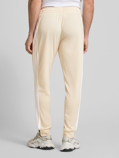 Männermodel trägt Regular Fit Sweat-Anzug mit Kontraststreifen von adidas Sportswear in Beige mit weißen Streifen, Ganzkörperansicht Rückansicht.