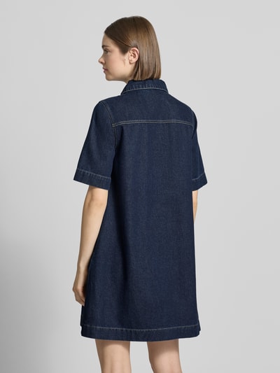 Frauenmodel trägt Jeanskleid mit Reißverschluss Modell 'AMARA KLARA' von JJXX, dunkelblau, Baumwoll-Viskose-Mix, A-Linie, Minikleid, Hemdblusenkragen, Brusttasche, Rückenlänge 85 cm bei Größe S, Brustweite 47 cm, Ärmellänge 28 cm, Ganzkörperansicht Rückansicht.