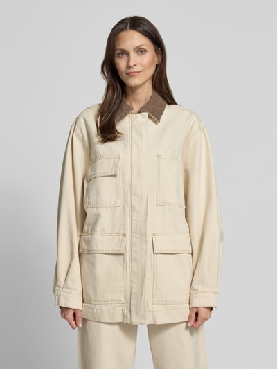Frauenmodel trägt Oversized Jeansjacke aus reiner Baumwolle Modell 'WORKWEAR CANVAS' von Armedangels in Beige mit braunem Umlegekragen, unifarben, große Taschen und sichtbare Nähte, Material Denim, Ganzkörperansicht von vorne.