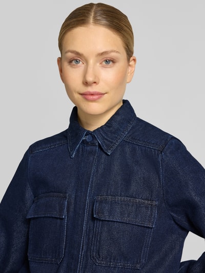 Kobiece modelka nosi Jeansbluse mit Brusttaschen und Kentkragen od Stefanel, bawełniany miks, krój regular fit, kieszenie z patkami, długi rękaw, ukryta lista guzików, sportowe mankiety, kolor granatowy, zbliżenie na górną część ciała.