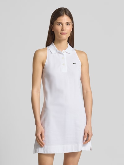 Frauenmodel trägt weißes Slim Fit Polokleid aus Baumwoll-Mix von Lacoste Sport mit Logo-Detail, Piqué-Struktur, Mini-Länge, Ganzkörperansicht von vorne.