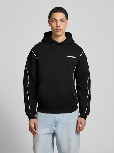 Męski model nosi Hoodie mit Logo und Känguru-Tasche von REVIEW, czarny, bawełniany krój regular fit, logo, kieszeń, przód, ujęcie całopostaciowe